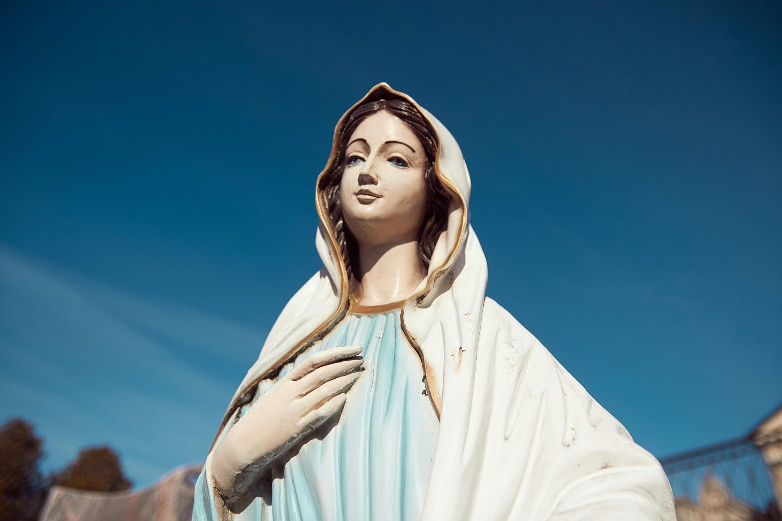 A serene statue of the Virgin Mary stands against a clear blue sky, symbolizing peace and faith.